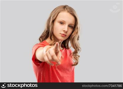 accusing gesture and people concept - teenage girl with long hair in red t-shirt pointing finger to you over grey background. teenage girl in red t-shirt pointing finger to you