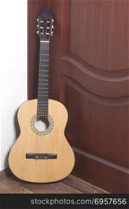 Acoustic guitar leaning against a wooden door. Acoustic guitar leaning against a wooden door in room