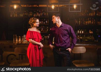 Acquaintance in bar, beautiful woman in red dress flirts with man behind counter. Date in nightclub, attractive couple funs together indoors. Acquaintance in bar, woman flirts with man