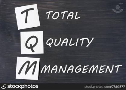 Acronym of TQM for total quality management - white chalk handwriting and sticky notes on a blackboard