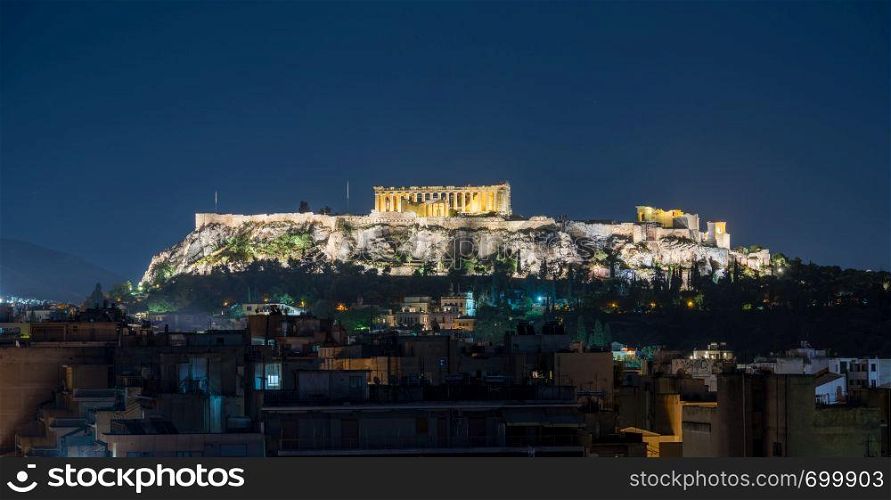 Acropolis hill at night with the city of Athens surrounding it. Acropolis hill rises above Athens apartments