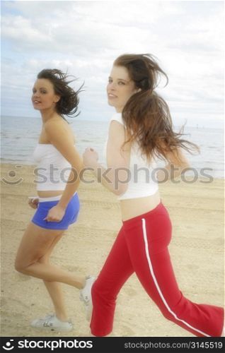 Action shot of two Young Australian women running and happily laughing along the beach at port Melbourne.