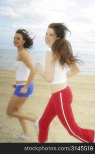 Action shot of two Young Australian women running and happily laughing along the beach at port Melbourne.