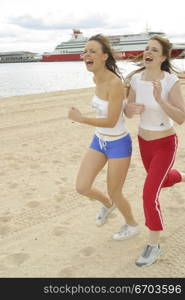 Action shot of two Young Australian women running and happily laughing along the beach at port Melbourne.