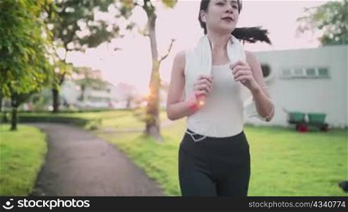 active asian woman wear white sport clothing running alone inside public park at sunset, relaxing jog, protection from virus, holding protective face mask, covid19 pandemic, human vitality wellness