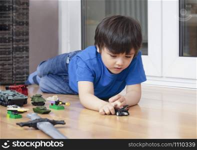 Active boy crawling on floor playing with soldiers and tank toys in playroom, Happy Kid playing wars and peace on his own, Child relaxing at home on weekend, Children imagination and development