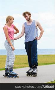 Active holidays, exercises, relationship concept. Woman and man wearing rollerskates standing and looking at each other, man touching her hips.. Couple wearing rollerskates looking at each other