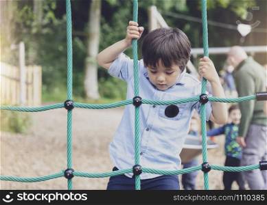 Active kid climbing rope in the playground,, Child enjoying activity in a climbing adventure park on summer sunny day, Cute little boy having fun on a playground outdoors.
