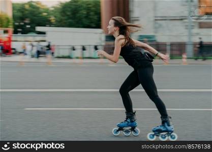 Active leisure concept. Full length shot of young slim woman rollerblades along asphalt on street enjoys speed spends free time on favorite hobby poses outdoors breathes fresh air. Rollerskating