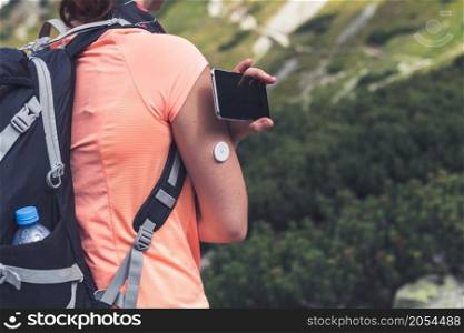 Active life of diabetics, woman hiking and checking glucose level with a remote sensor and mobile phone, sensor checkup glucose levels without blood. Diabetes treatment. Purple toned image.. Active life of diabetics, woman hiking and checking glucose level with a remote sensor and mobile phone