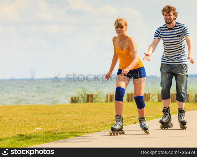 Active lifestyle people and freedom concept. Young fit couple on roller skates riding outdoors on sea coast, woman and man rollerblading enjoying time together