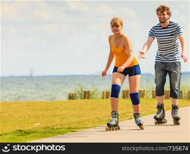 Active lifestyle people and freedom concept. Young fit couple on roller skates riding outdoors on sea coast, woman and man rollerblading enjoying time together
