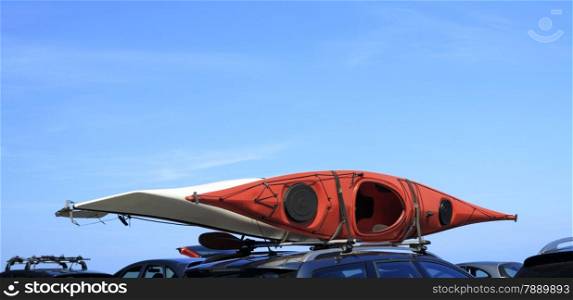 Active lifestyle sport concept - car with kayak red canoe on top roof blue sky background with copy space.