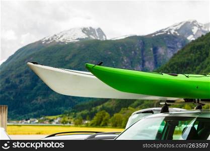 Active lifestyle sport concept. Car with two canoes white and green on top roof, mountains landscape in the background. Car with two canoes on top roof in mountains
