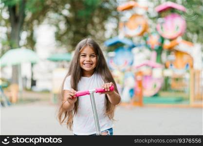 Active little child girl riding scooter on road in park outdoors on summer day