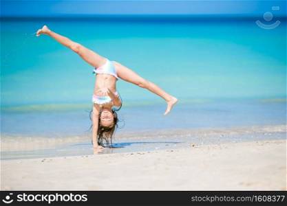 Active little girl at beach having a lot of fun. Cute kid making sporty exercises on the seashore. Adorable active little girl at beach during summer vacation