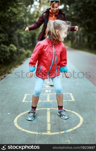 Active little girl playing hopscotch on playground outdoors. Jumping for joy. Children outdoor activities
