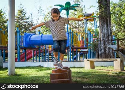 Active little girl walking on balance beam in the outdoor playground in the park. Happy child girl having fun in children playground. Play is learning in childhood.
