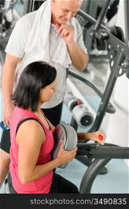 Active man watch personal instructor adjust machine level at gym