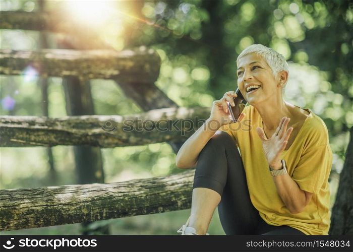 Active mature woman taking a break on a fitness trail, talking over the phone. Active Mature Woman Taking a Fitness Break
