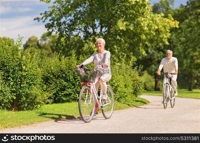 active old age, people and lifestyle concept - happy senior couple riding bicycles at summer park. happy senior couple riding bicycles at summer park