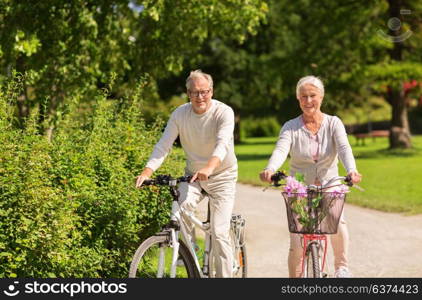 active old age, people and lifestyle concept - happy senior couple riding bicycles at summer park. happy senior couple riding bicycles at summer park