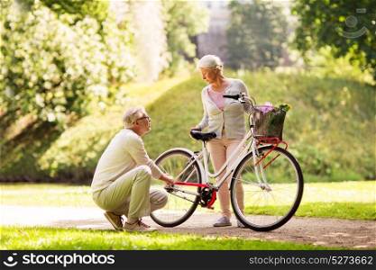 active old age, people and lifestyle concept - happy senior couple with fixie bicycle at summer city park. happy senior couple with bicycle at summer park