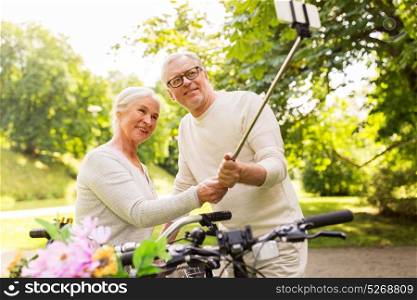 active old age, technology and lifestyle concept - happy senior couple walking with fixie bicycles taking selfie by smartphone at summer park. senior couple with bicycles taking selfie at park