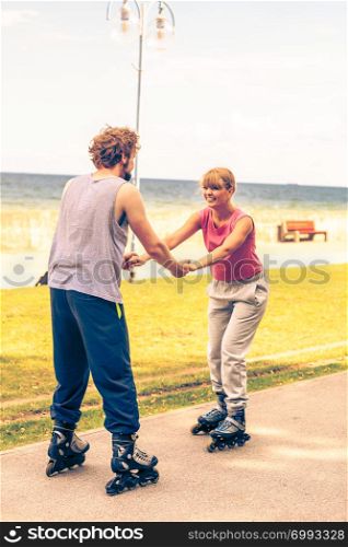 Active people friends in training suit rollerskating outdoor. Woman and man couple holding hands riding enjoying sport.. Active people friends rollerskating outdoor.