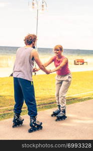 Active people friends in training suit rollerskating outdoor. Woman and man couple holding hands riding enjoying sport.. Active people friends rollerskating outdoor.