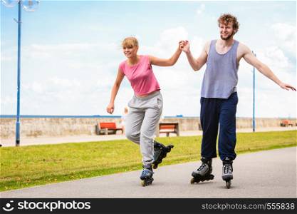 Active people modern couple exercise together and have fun. Relaxing hobby. Young people hold hands while rollerblading in park.. Young couple rollerblading in park holding hands.