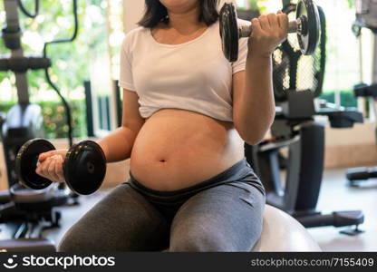 Active pregnant woman exercise in fitness center at yoga room. The young expecting mother holding baby in pregnant belly. Maternity prenatal care and woman pregnancy concept.