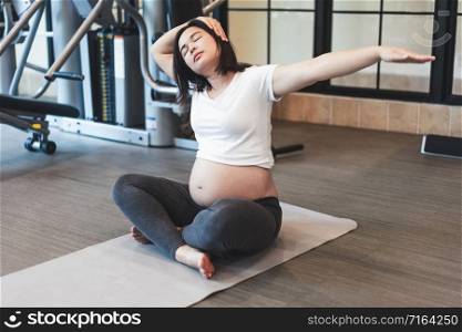 Active pregnant woman exercise in fitness center at yoga room. The young expecting mother holding baby in pregnant belly. Maternity prenatal care and woman pregnancy concept.
