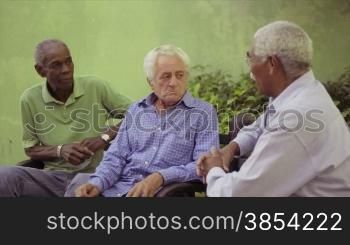 Active retired elderly people and free time, group of happy senior african american and caucasian male friends talking and sitting on bench in park. Sequence