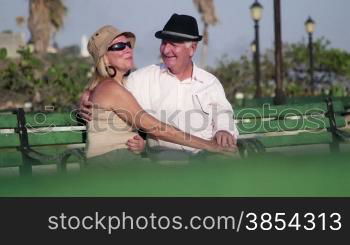 Active retired people with husband and wife relaxing, senior man and woman talking and kissing in city park. Sequence