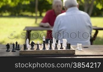 Active retirement, old friends and leisure, two senior men having fun and playing chess game at park. Rack focus from players to chessboard