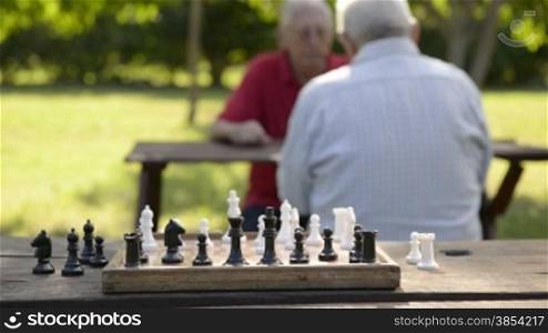 Active retirement, old friends and leisure, two senior men having fun and playing chess game at park. Rack focus from players to chessboard