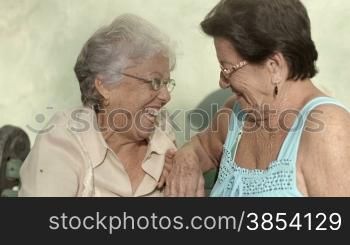 Active retirement, two elderly female friends talking and laughing on bench in public park