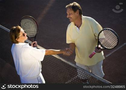 Active senior couple is shaking hands on the tennis court with tennis rackets in hand. Outdoor, sunlight.