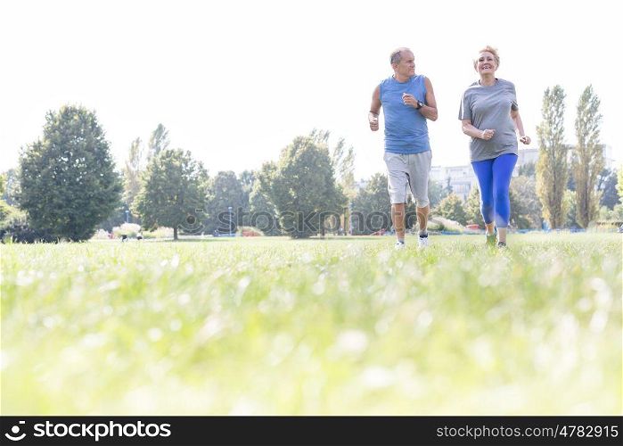 Active senior couple jogging on grassy field at park