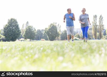 Active senior couple jogging on grassy field at park