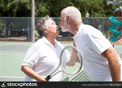 Active senior couple kissing on the tennis court.