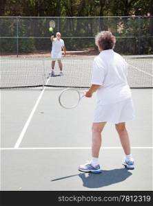Active senior couple playing tennis together on an outdoor court