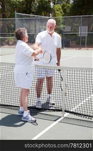Active senior couple shakes hands over the tennis net.