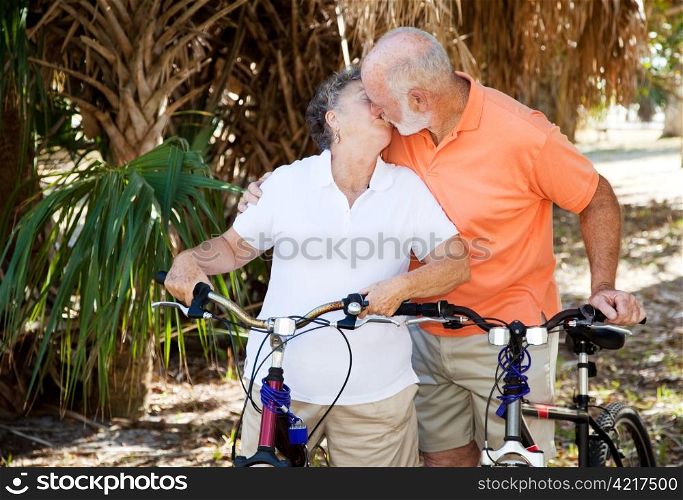 Active senior couple taking a breat from cycling to kiss each other.