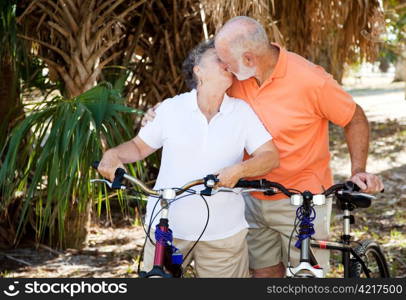 Active senior couple taking a breat from cycling to kiss each other.