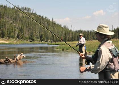 Active senior couple wading in the Firehole River (Yellowstone National Park) and fly-fishing for trout.