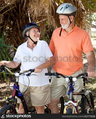 Active senior couple with their bicycles, looking lovingly at each other.