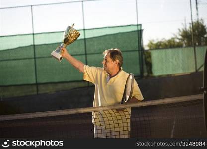 Active senior man in his 70s is posing on the tennis court with tennis racket in hand. Outdoor, sunlight.