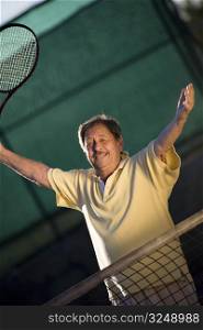 Active senior man in his 70s is posing on the tennis court with tennis racket in hand. Outdoor, sunlight.